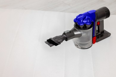 Photo of Modern vacuum cleaner on white mattress indoors. Space for text
