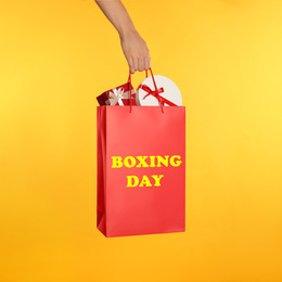 Image of Woman holding red shopping bag with text Boxing Day full of gifts on yellow background, closeup