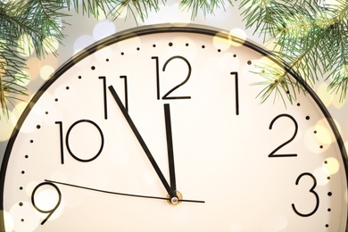 Image of Clock showing five minutes till midnight with fir tree branches, closeup with bokeh effect. New Year countdown