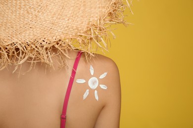 Teenage girl with sun protection cream on her back against yellow background, closeup