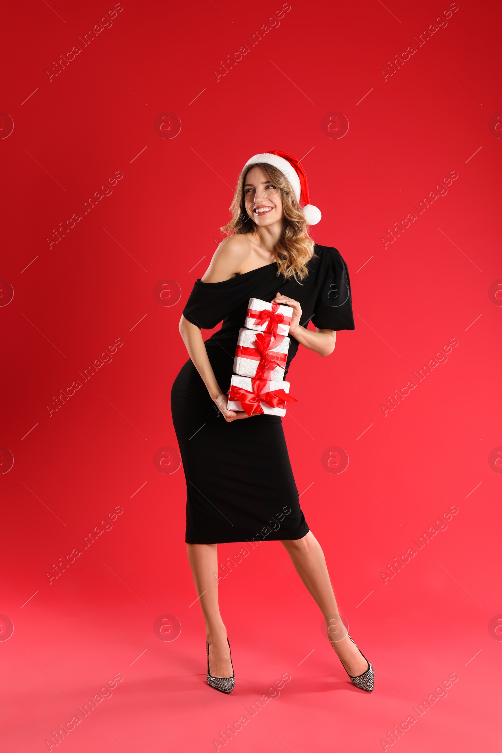 Photo of Beautiful young woman in Santa hat with Christmas presents on red background