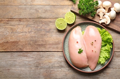 Flat lay composition with raw chicken breasts and ingredients on wooden background. Space for text