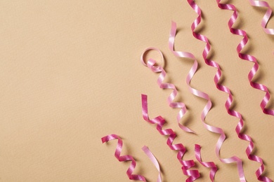 Shiny pink serpentine streamers on beige background, flat lay. Space for text