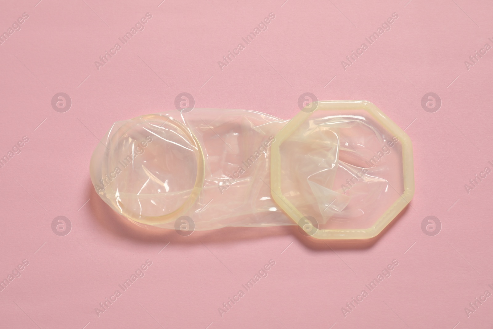 Photo of Unrolled female condom on light pink background, above view. Safe sex