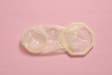 Unrolled female condom on light pink background, above view. Safe sex