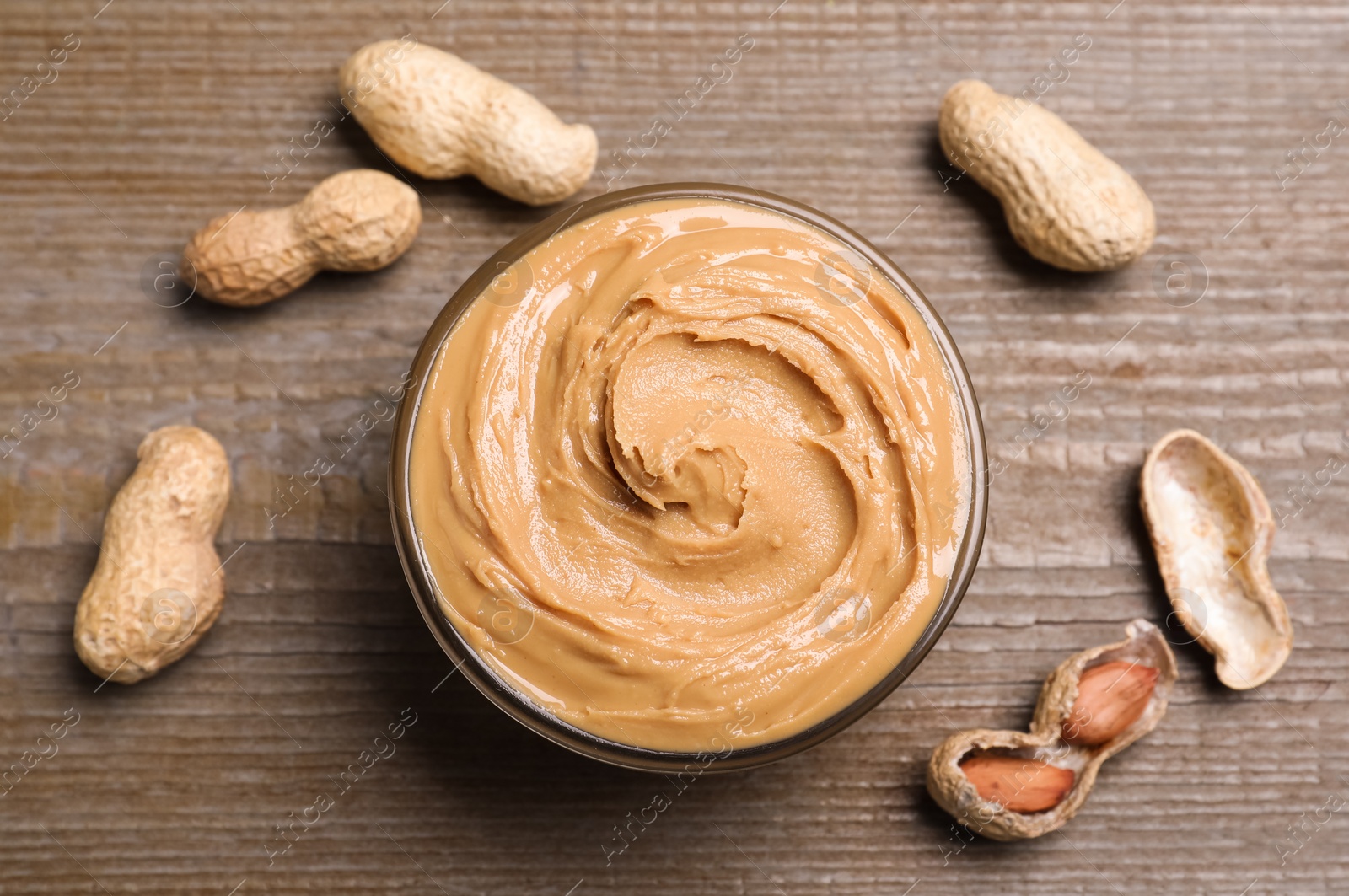 Photo of Yummy peanut butter in glass bowl on wooden table, flat lay