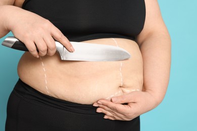 Photo of Obese woman with knife and marks on body against light blue background, closeup. Weight loss surgery