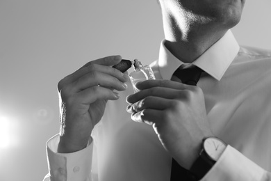 Photo of Handsome man applying perfume on neck against light background, closeup. Black and white effect