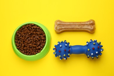 Photo of Pet toy, dog treat and bowl of food on yellow background, flat lay