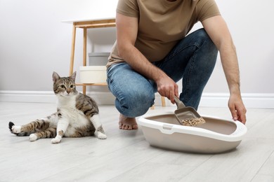 Photo of Young man cleaning cat litter tray at home, closeup