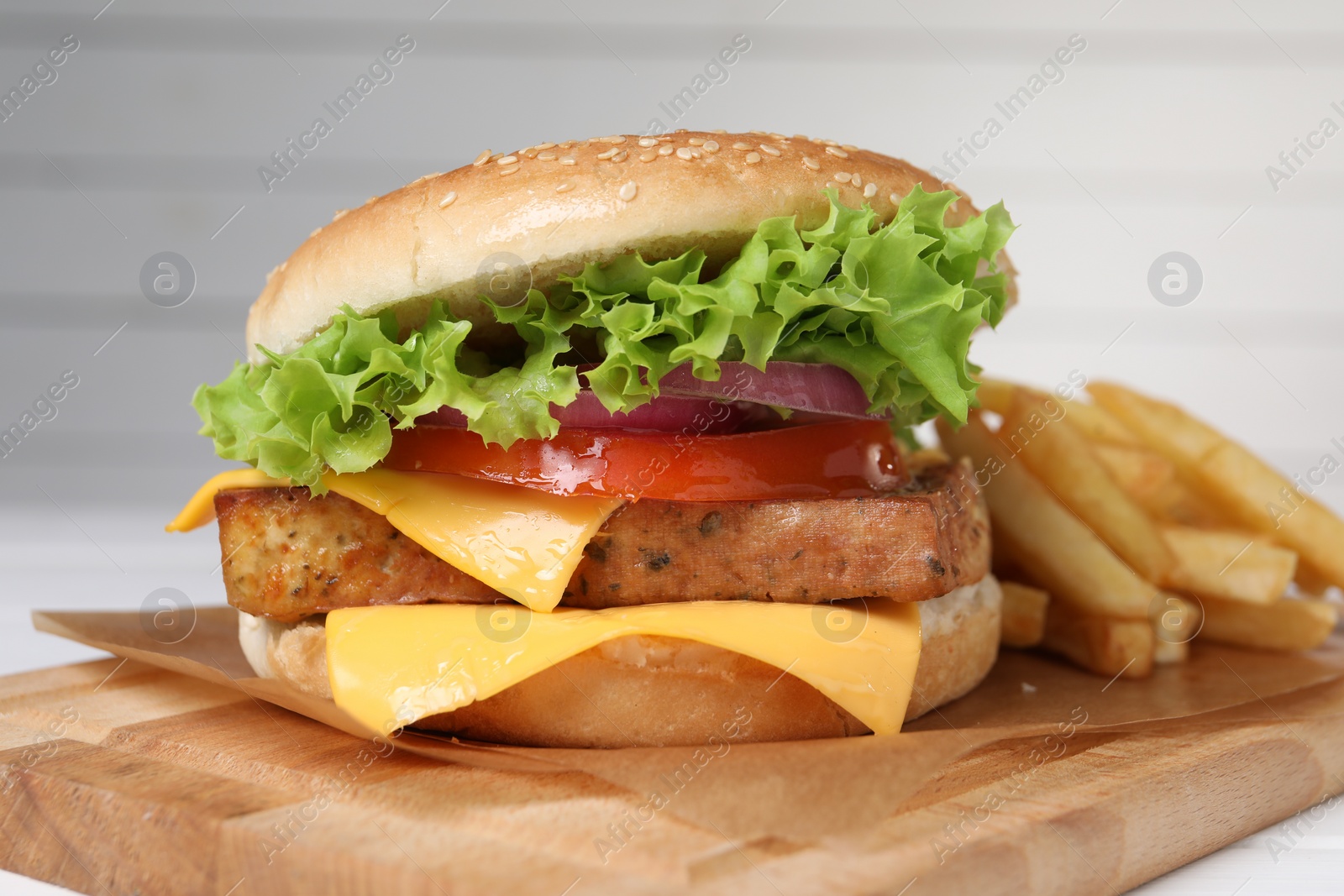 Photo of Delicious tofu burger served with french fries on wooden board, closeup