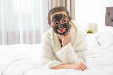 Photo of Young woman with clay mask on her face in bedroom