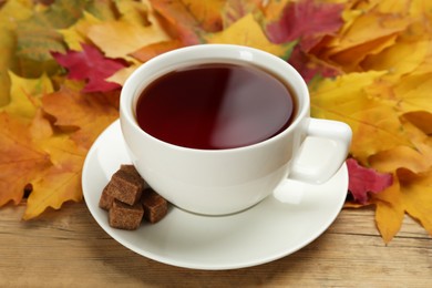 Cup of hot tea and autumn leaves on wooden table, closeup