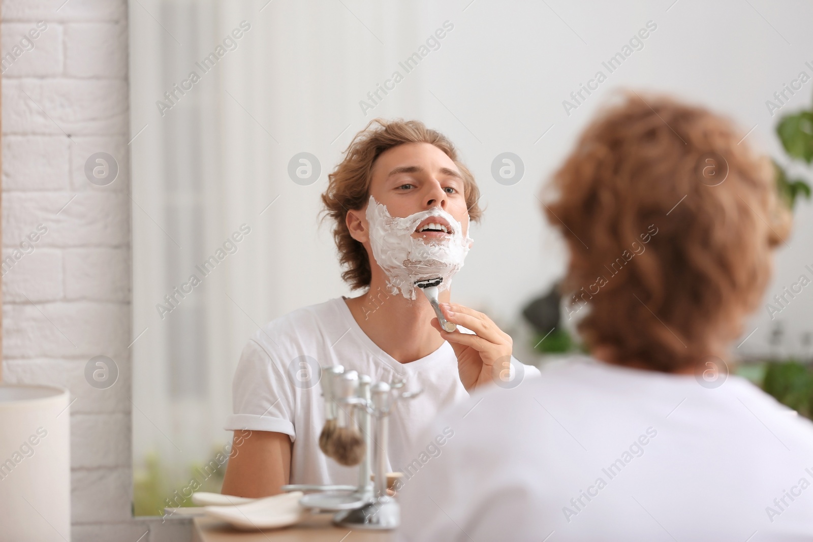 Photo of Young handsome man shaving in bathroom