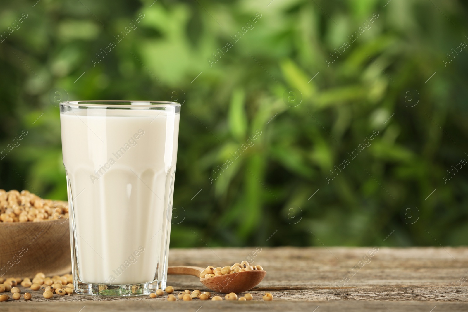 Photo of Glass with fresh soy milk and grains on white wooden table against blurred background. Space for text