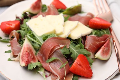 Photo of Tasty salad with brie cheese, prosciutto, strawberries and figs on white plate, closeup