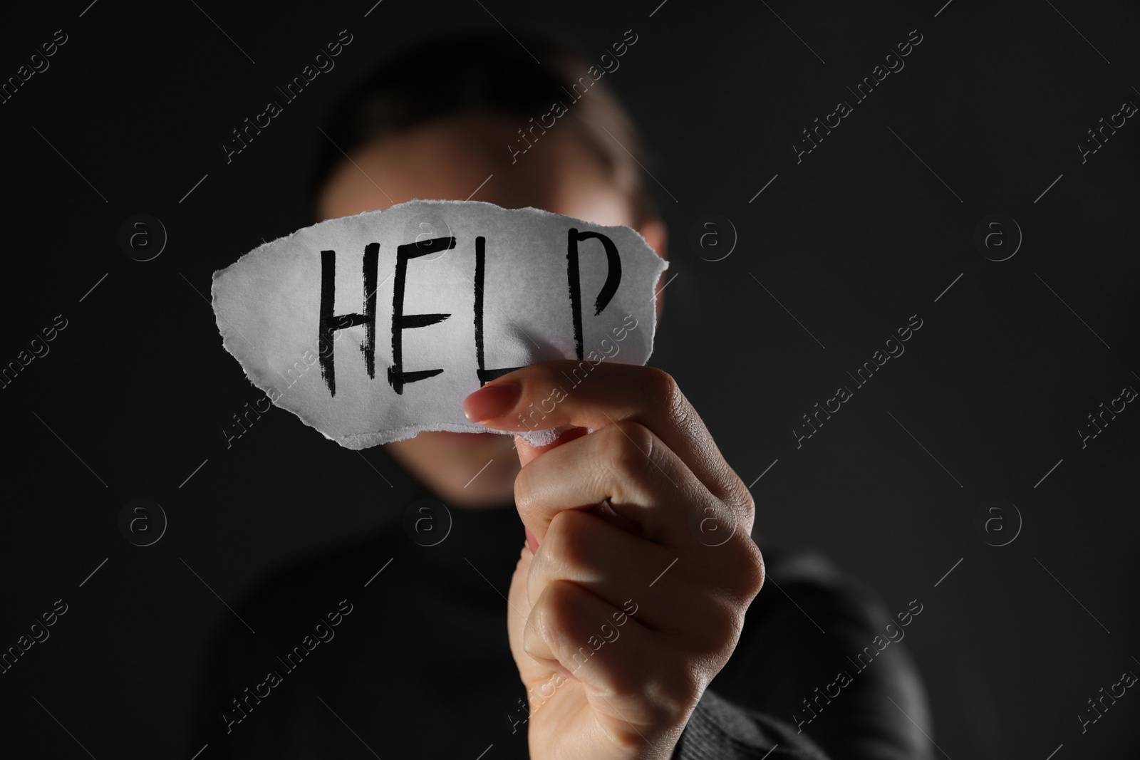 Photo of Woman holding piece of paper with word Help on black background, closeup. Domestic violence concept