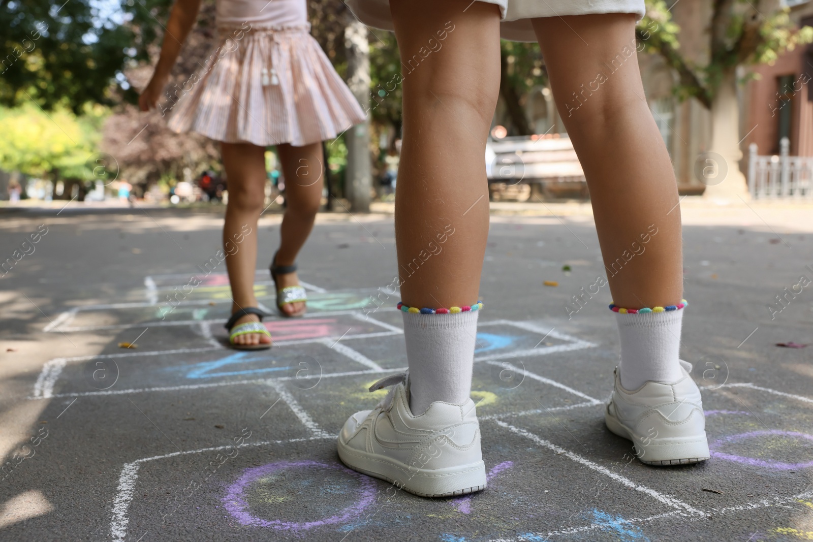 Photo of Little children playing hopscotch drawn with chalk on asphalt outdoors, closeup