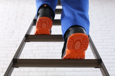 Professional worker climbing up ladder against white brick wall, low angle view