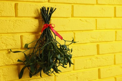Mistletoe bunch with red bow hanging on yellow brick wall, space for text. Traditional Christmas decor