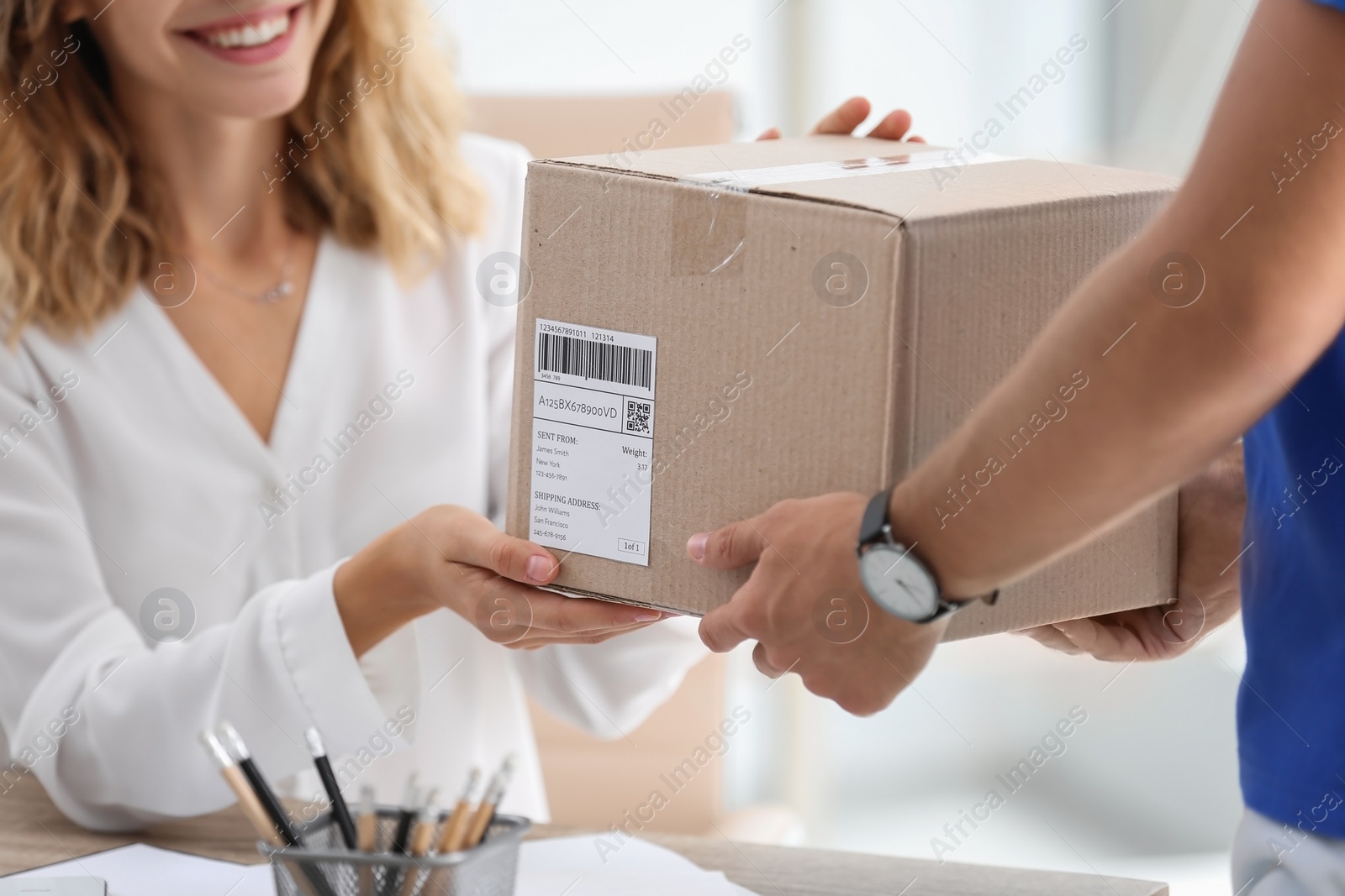 Photo of Young woman receiving parcel from courier in office