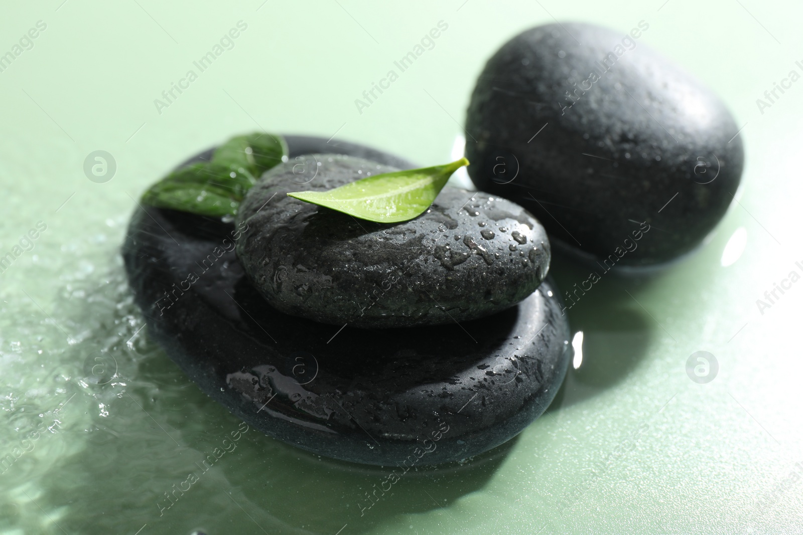 Photo of Spa stones and fresh leaves on light green background, closeup