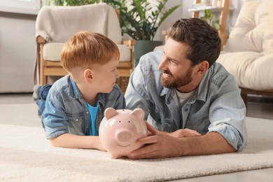 Photo of Father and his son with ceramic piggy bank on floor at home