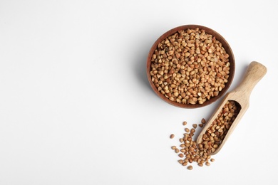 Bowl and scoop with uncooked buckwheat on white background, top view