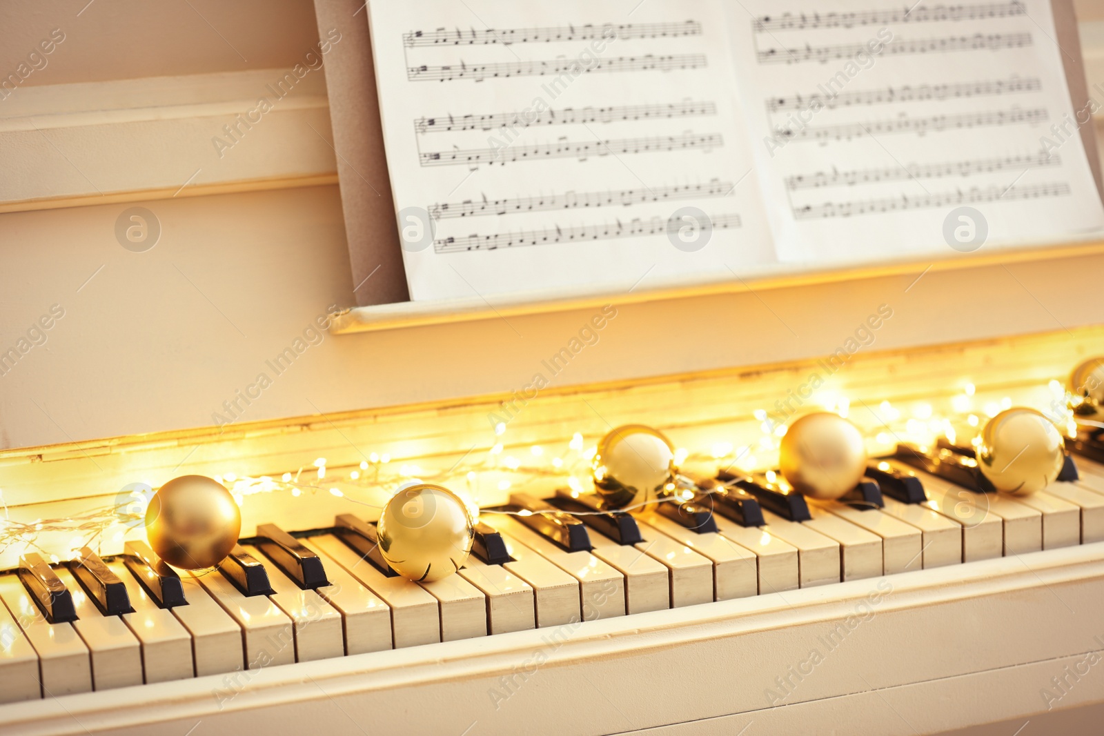 Photo of Golden baubles and fairy lights on piano keys, closeup. Christmas music