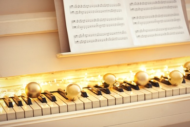Photo of Golden baubles and fairy lights on piano keys, closeup. Christmas music