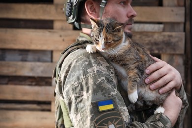 Photo of Ukrainian soldier rescuing stray cat outdoors. Space for text