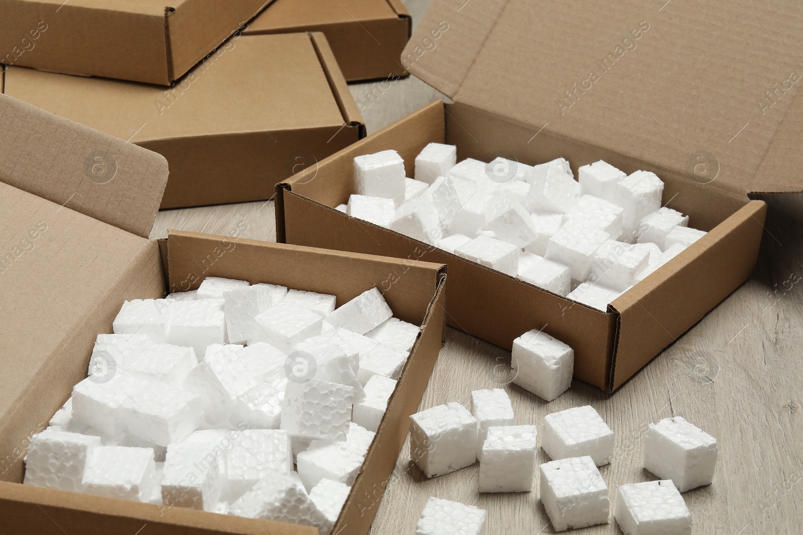 Photo of Open cardboard boxes with pieces of polystyrene foam on wooden floor. Packaging goods