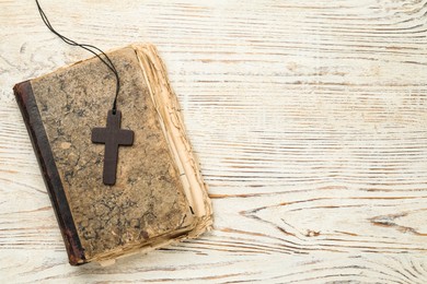 Photo of Wooden Christian cross and old Bible on white table, top view. Space for text