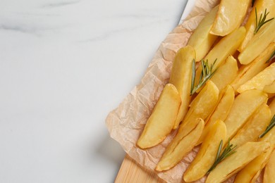 Photo of Tasty baked potato wedges and rosemary on white marble table, top view. Space for text
