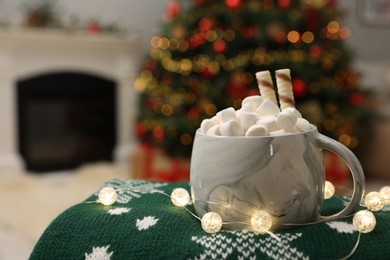 Christmas cocoa with marshmallows and wafer sticks in cup on green sweater indoors, closeup. Space for text
