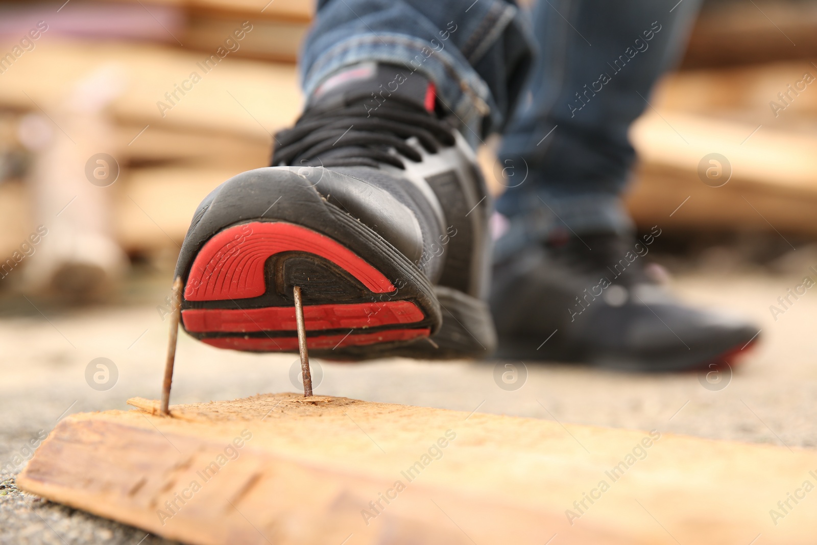 Photo of Careless worker stepping on nails in wooden plank outdoors, closeup