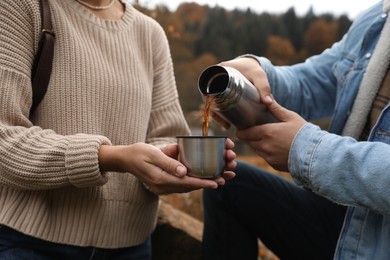 Boyfriend pouring hot drink from metallic thermos into cup lid for his girlfriend outdoors, closeup