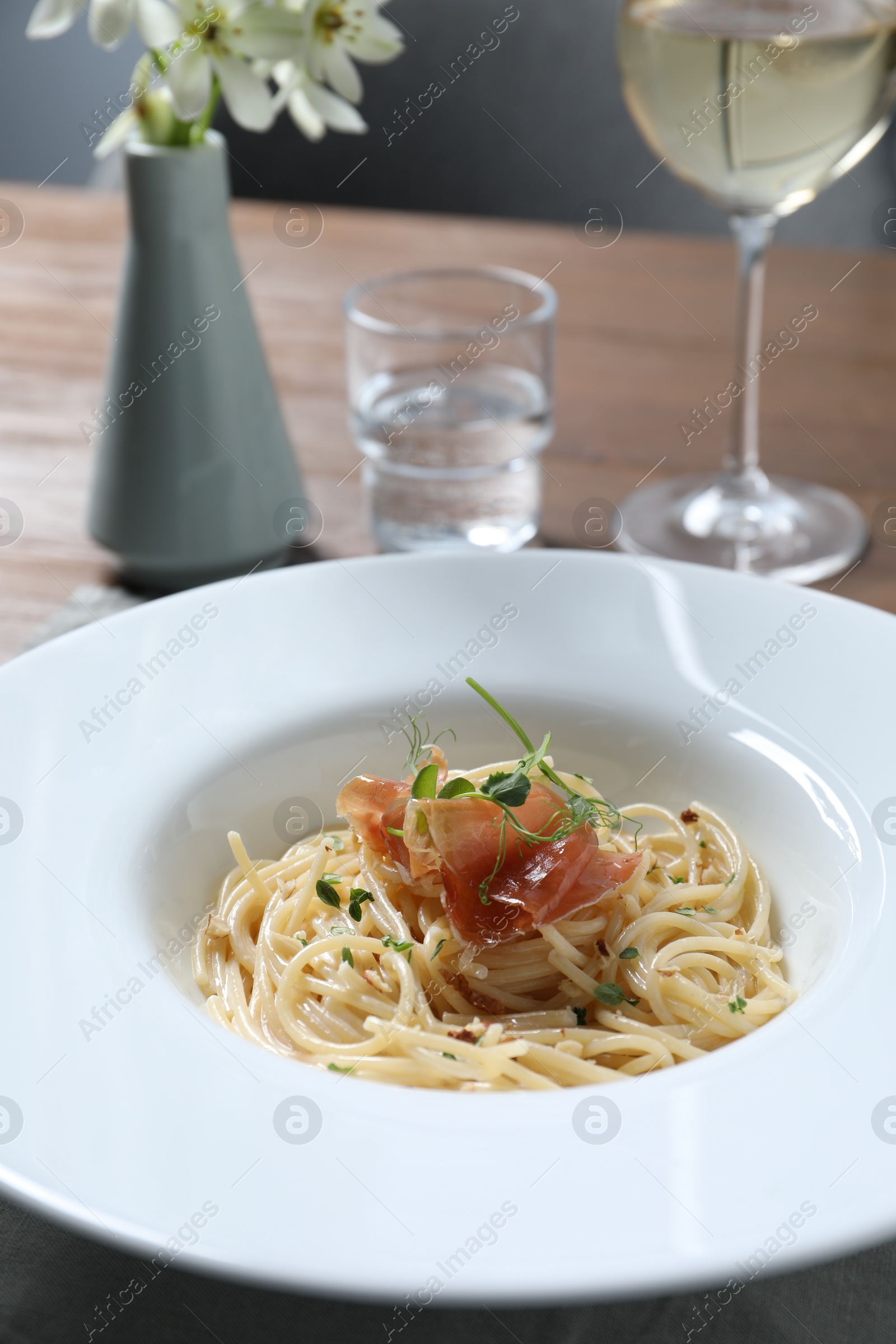 Photo of Tasty spaghetti with prosciutto and microgreens served on wooden table, closeup. Exquisite presentation of pasta dish