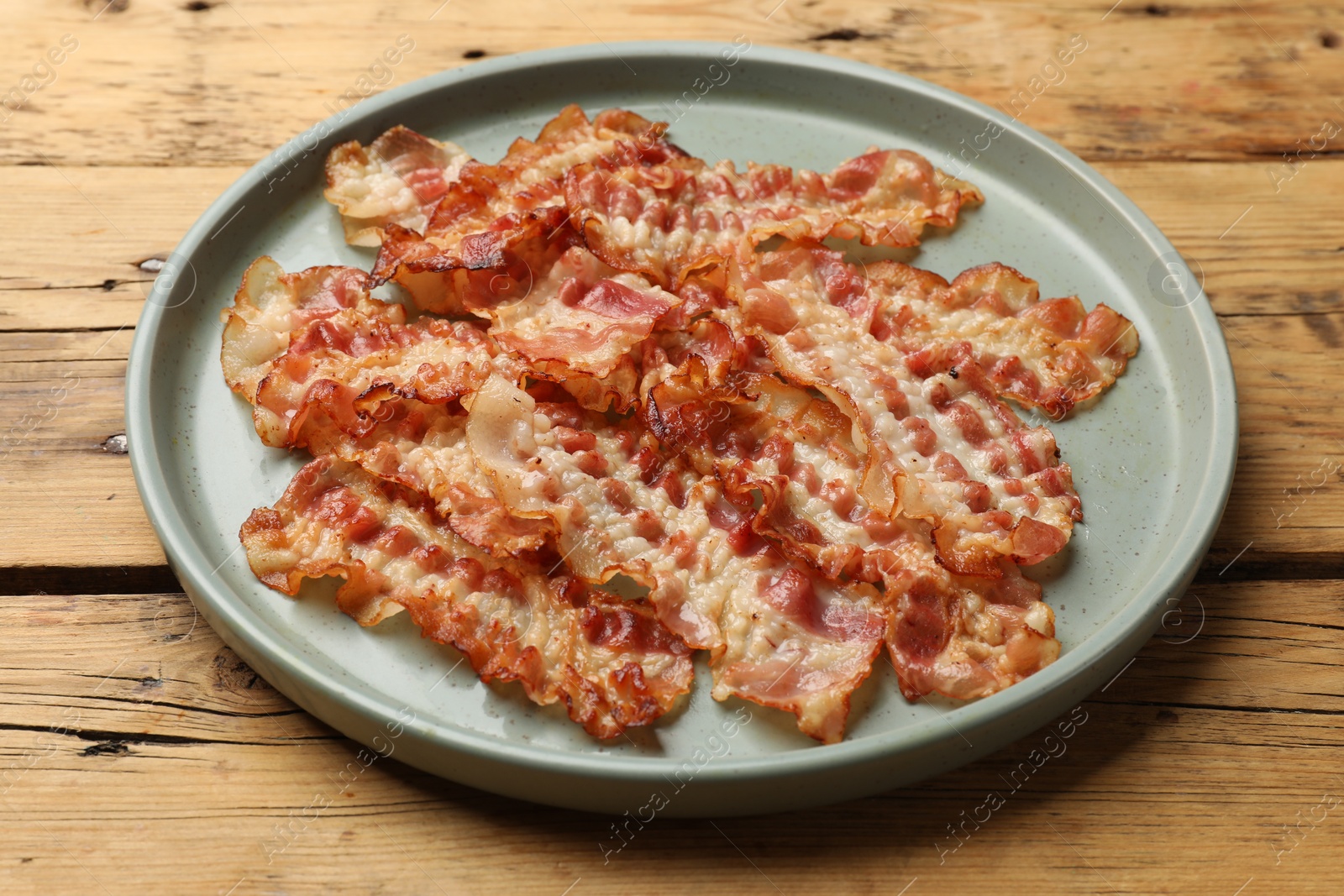 Photo of Delicious fried bacon slices on wooden table