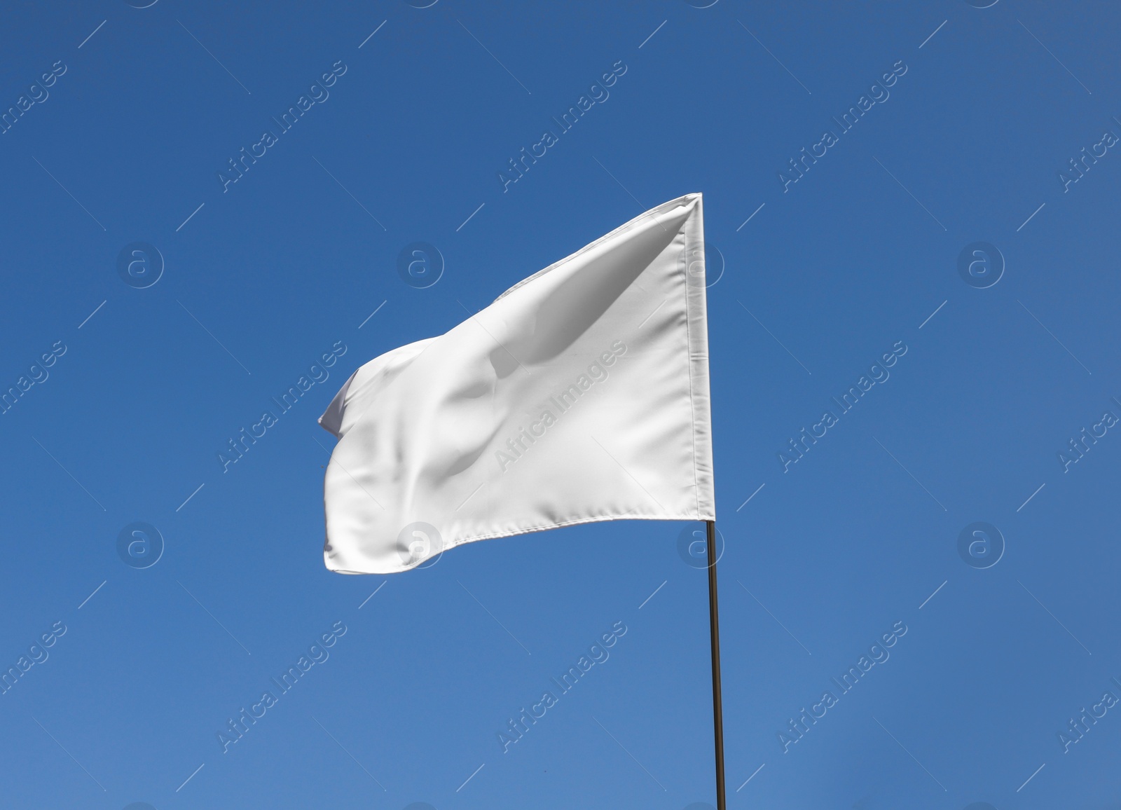 Photo of White flag fluttering against blue sky on sunny day