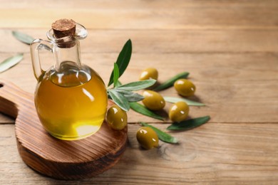 Photo of Jug of cooking oil, olives and green leaves on wooden table. Space for text