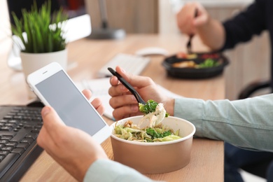 Photo of Office employee with smartphone having lunch at workplace, closeup. Food delivery