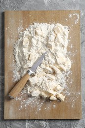 Photo of Making shortcrust pastry. Flour, butter, knife and wooden board on grey table, top view