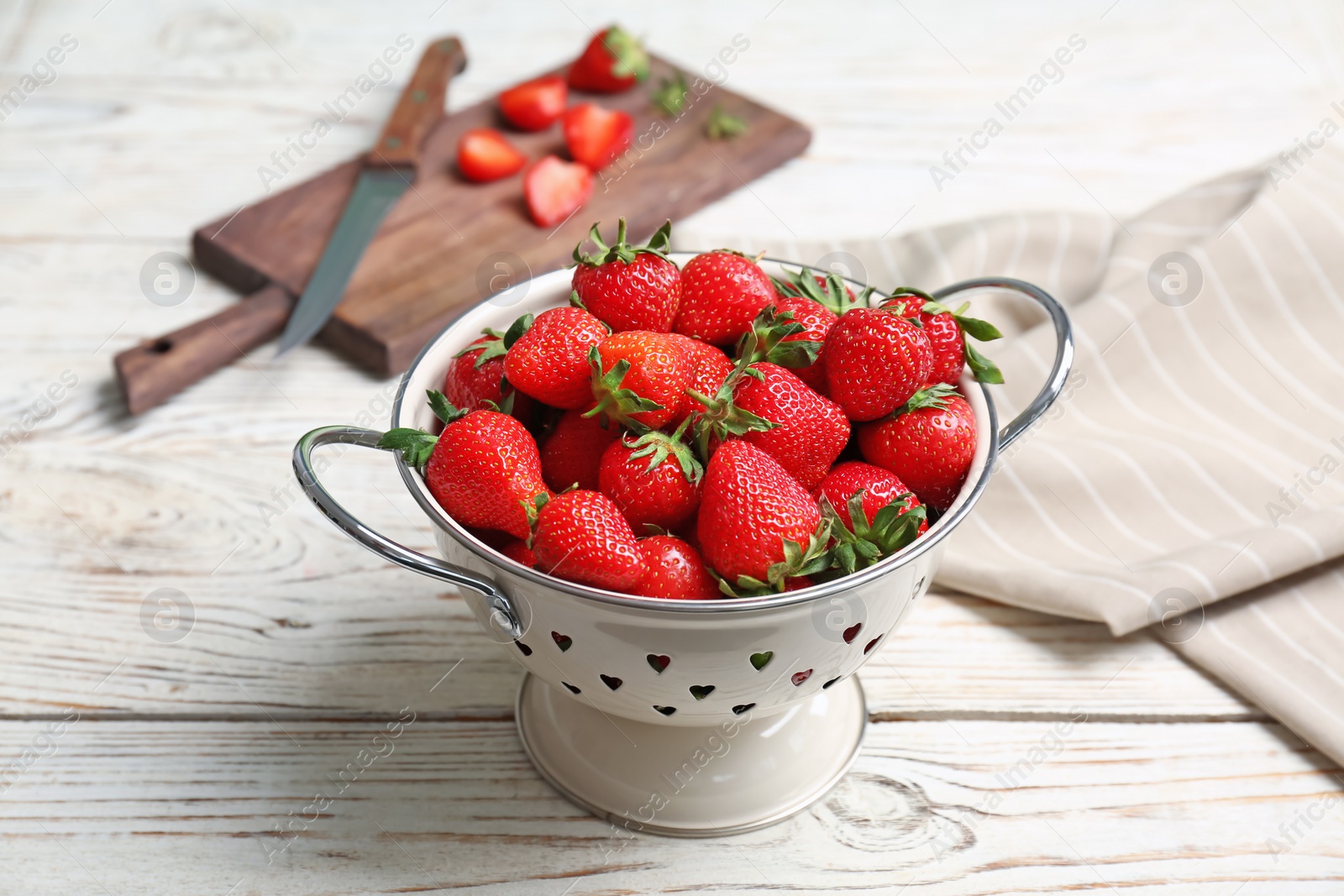 Photo of Colander with ripe red strawberries on wooden table