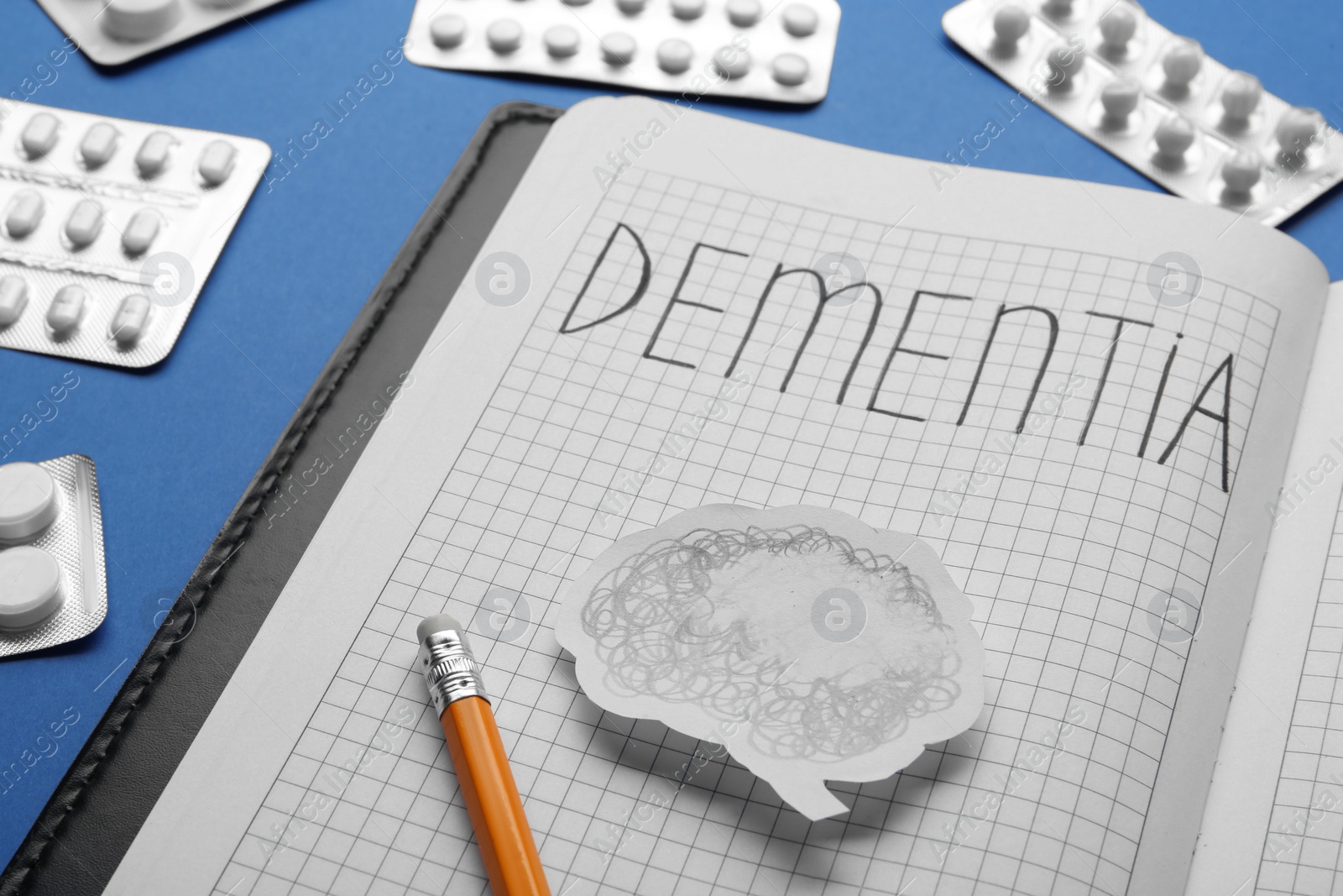 Photo of Notebook with word Dementia, brain cutout, pencil and pills on blue background, closeup