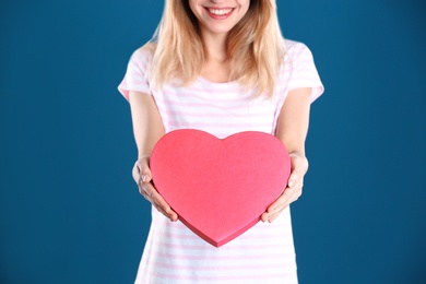 Photo of Woman with heart shaped gift box on color background, closeup