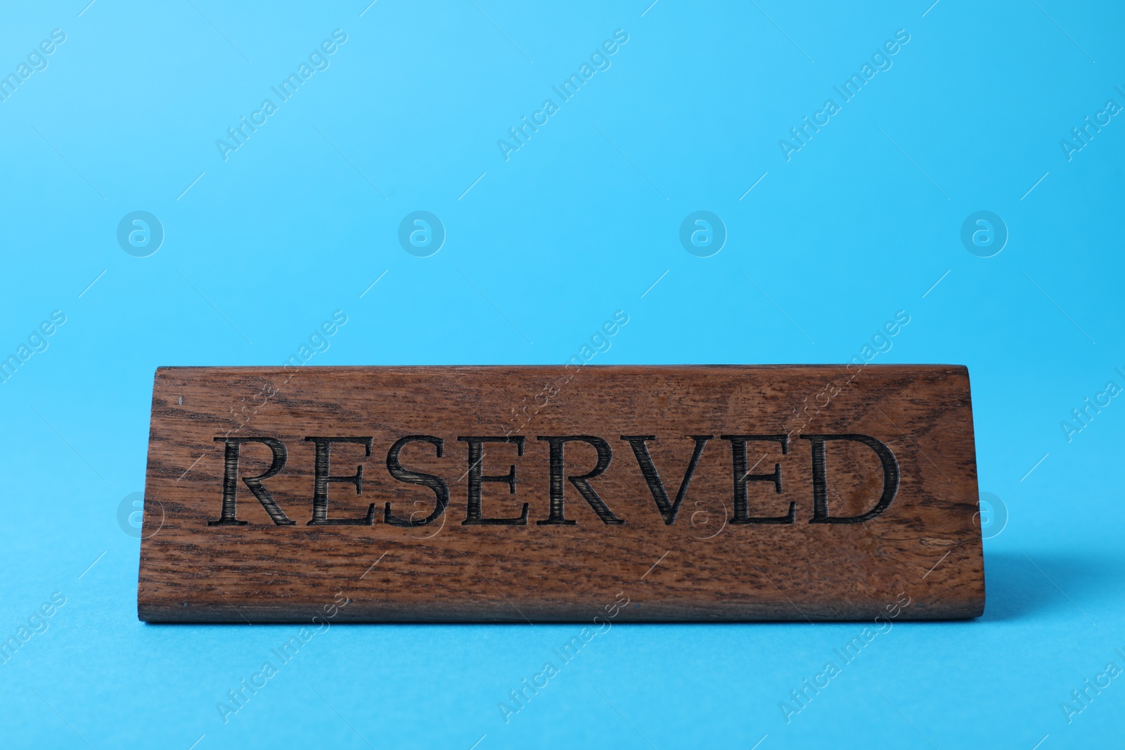 Photo of Elegant wooden sign Reserved on light blue background