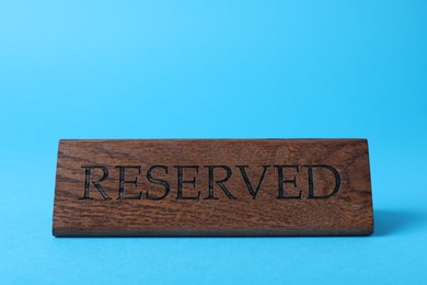 Photo of Elegant wooden sign Reserved on light blue background