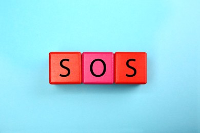 Photo of Abbreviation SOS (Save Our Souls) made of color cubes with letters on light blue background, top view