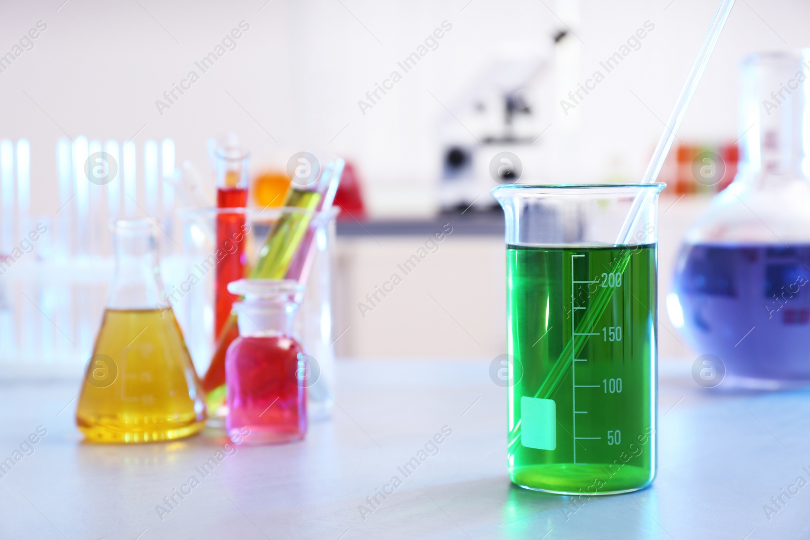 Photo of Beaker with color liquid on table against blurred background, space for text.  Chemistry glassware